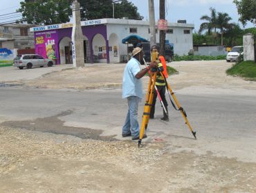 Surveyors working with tripod and equipment on a road.