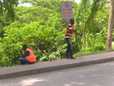 Two workers in orange vests near a no littering sign.