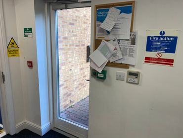 A glass door leading outside with safety and fire action signs on the wall.
