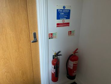 Two fire extinguishers next to a wooden door with fire action signs above.