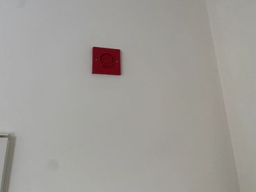 Red fire alarm mounted high on a white wall.