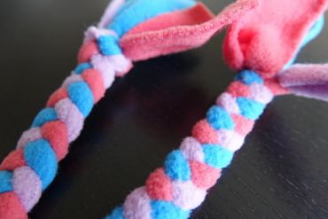 Close up of small plaited toy with 4 ends, lilac, turquoise and cerise pink.