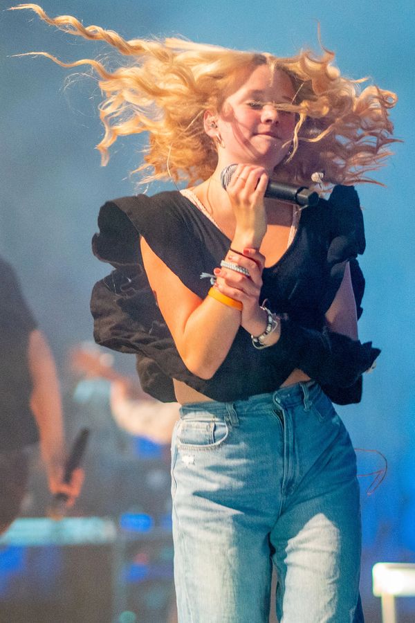 Teenage girl with blonde hair holding a microphone singing and dancing on stage at a concert.