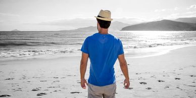 Man in blue shirt and hat standing on a black and white beach.