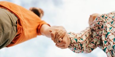 Couple holding hands against a cloudy sky, symbolizing connection and love.
