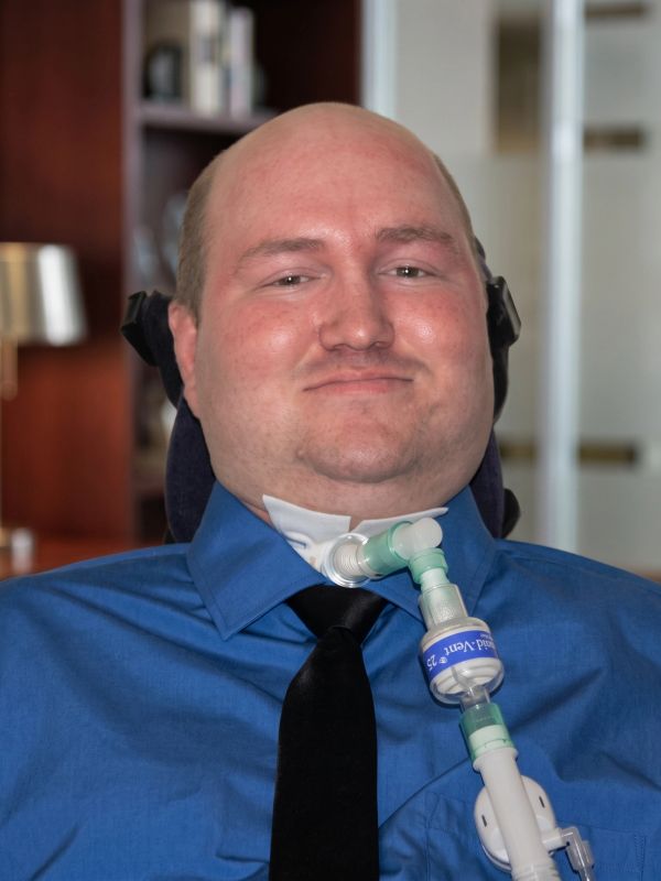 Man with ventilator in blue shirt and black tie.