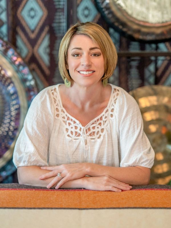 Smiling woman in white blouse sitting with hands folded.