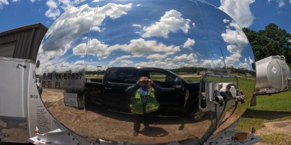 Reflection of a person and truck in a shiny spherical surface.