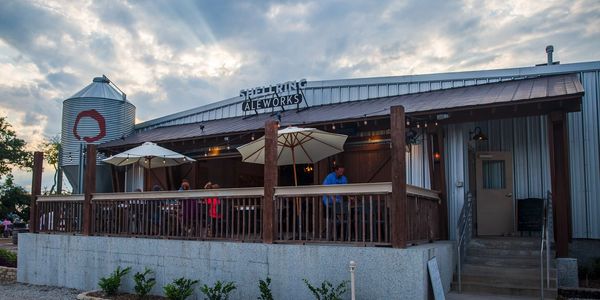 Exterior view of a brewery with outdoor seating under umbrellas at sunset.