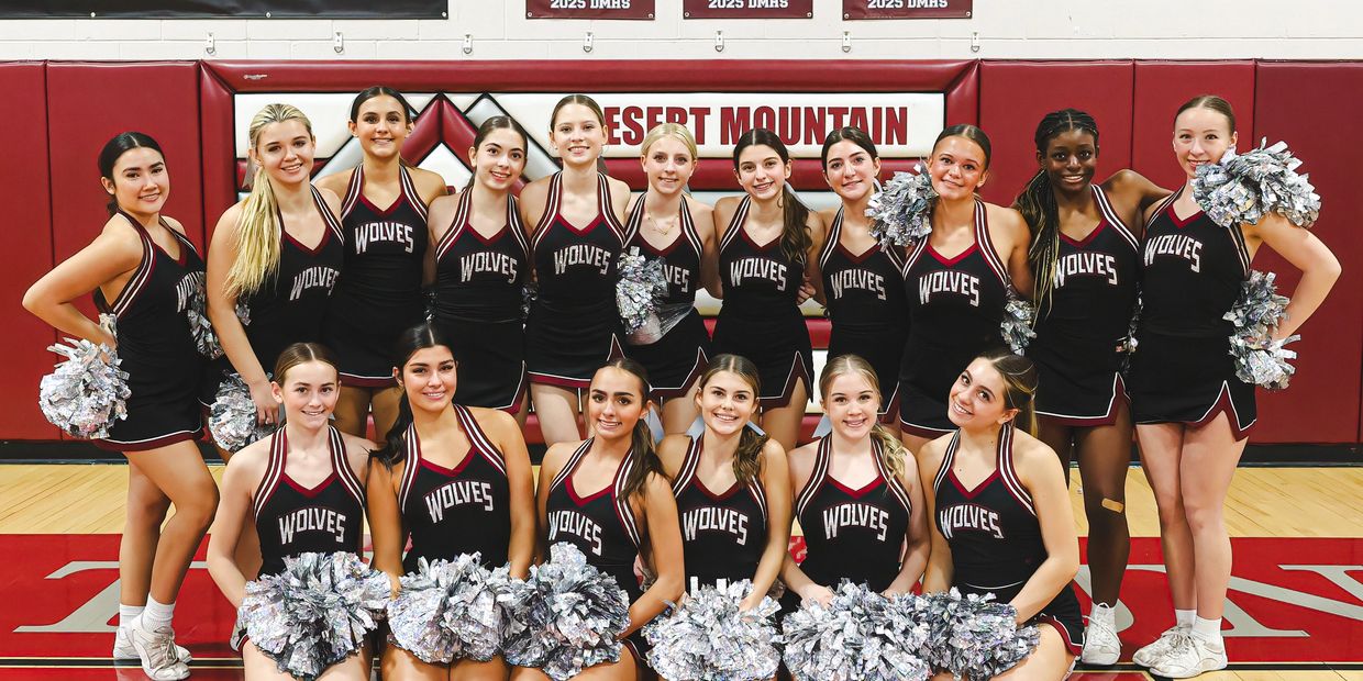 A high school cheerleading team posing in uniform on a basketball court.