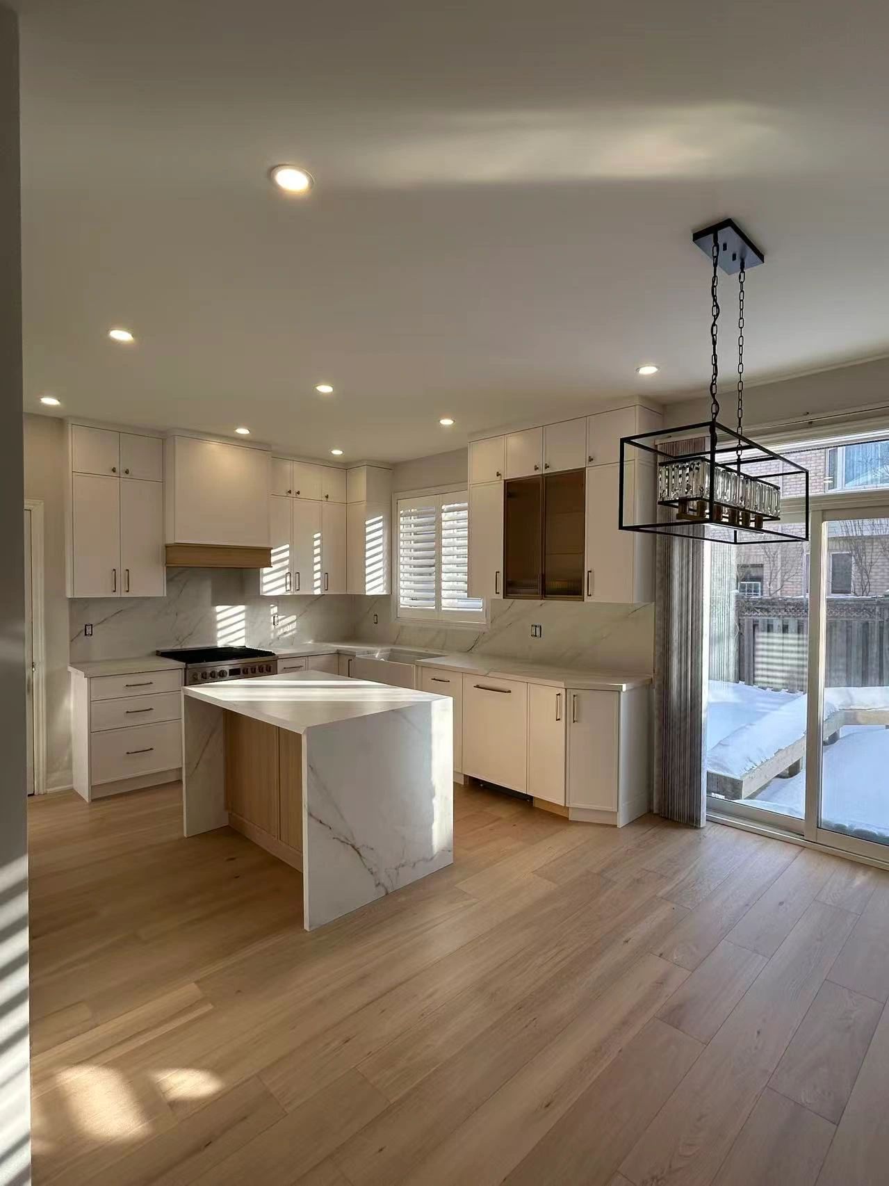 Modern kitchen with white cabinetry, marble island, and large window.
