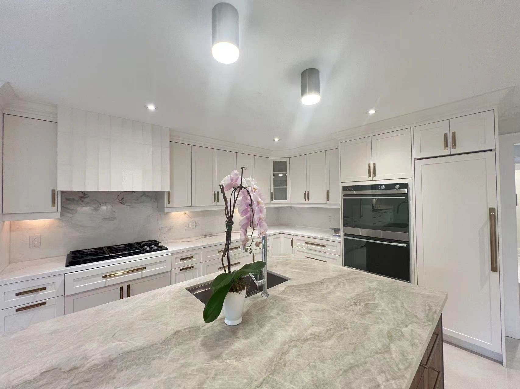Modern white kitchen with marble countertops and a pink orchid centerpiece.