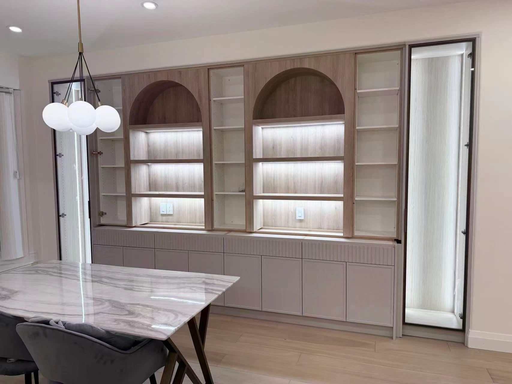 Modern dining area with illuminated wooden shelves and marble table.