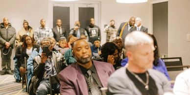 People attentively seated and standing in a room during an event or service.