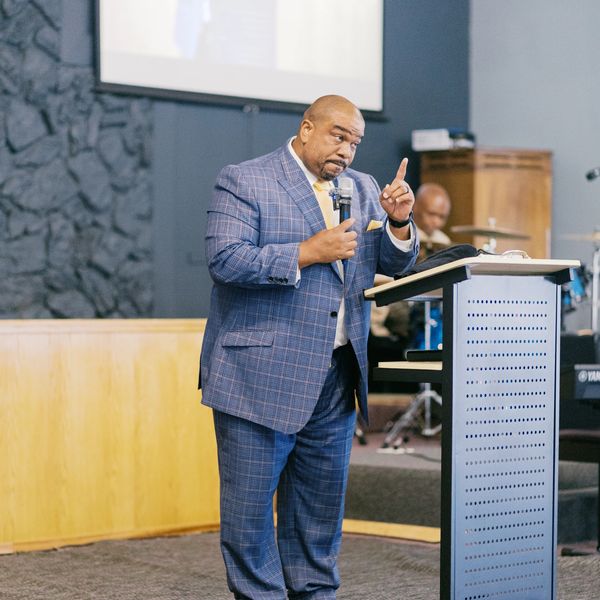 A man in a blue suit speaking with a microphone at a podium inside a church.