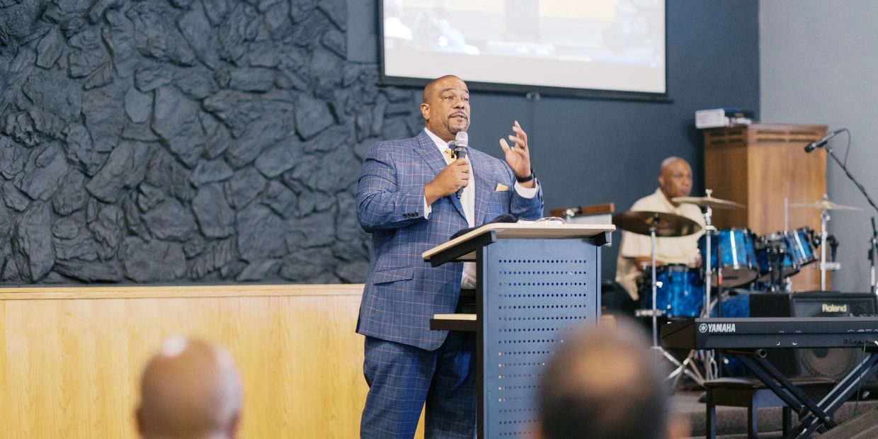 A man in a blue suit speaks at a podium in a church setting.