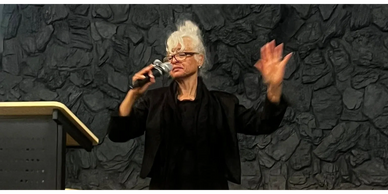 Woman with white hair speaks passionately into a microphone.