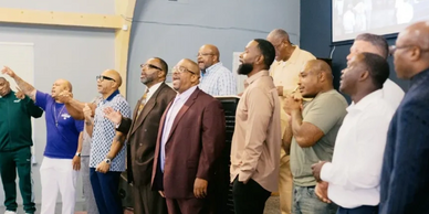 A group of men standing and singing together indoors.