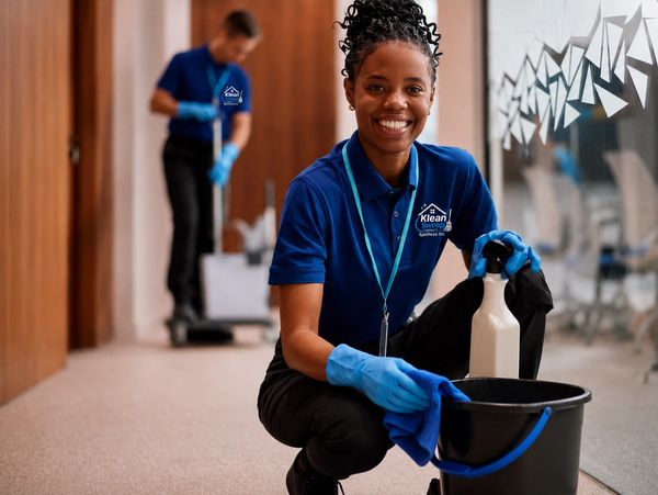 Smiling cleaner kneeling with cleaning supplies in office.