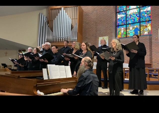 Members of Capella Nova singing in front of organ pipes with the pianist in front. 