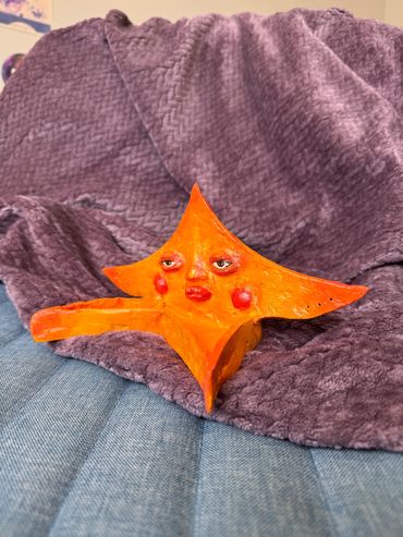 Orange starfish sculpture with a face on a purple blanket.