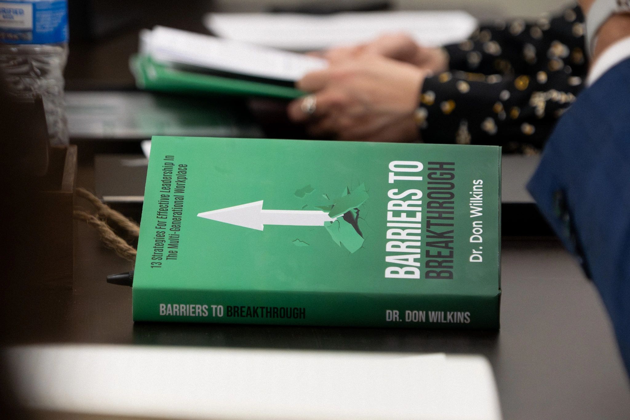 Green book titled 'Barriers to Breakthrough' by Dr. Don Wilkins on a table.