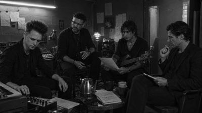 Four men in a music studio, discussing and reading notes.