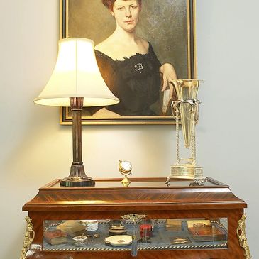 Elegant room corner with antique lamp, trophy, and portrait above a glass display cabinet.
