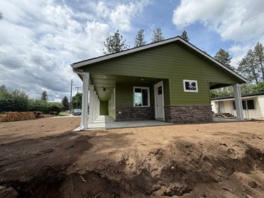 Newly built green house with stone accents and a spacious yard under a cloudy sky.
