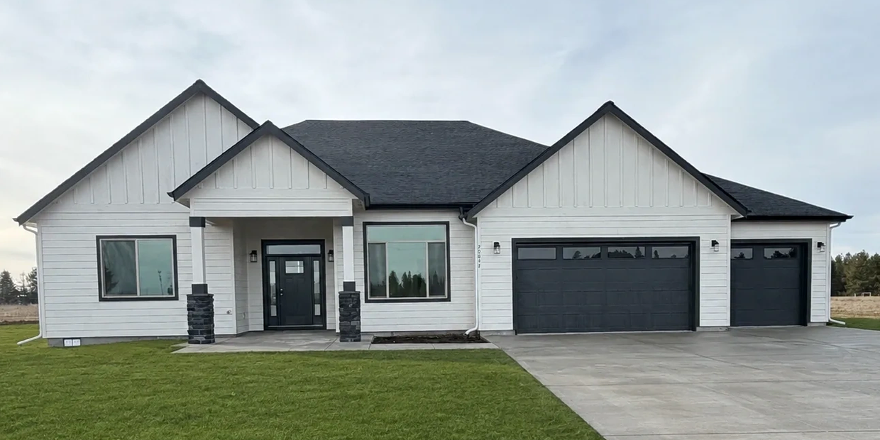Modern white house with black roof and garage doors.
