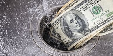 US dollar bills being disposed into a sink drain labeled 'INSINKERATOR'.