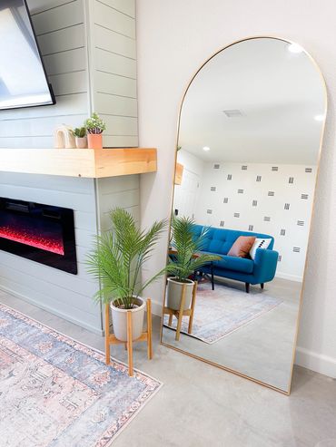 Elegant arched mirror reflecting a modern living room with a blue sofa and fireplace.