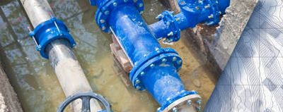 Hand drawing a water infrastructure plan beside blue water pipes.