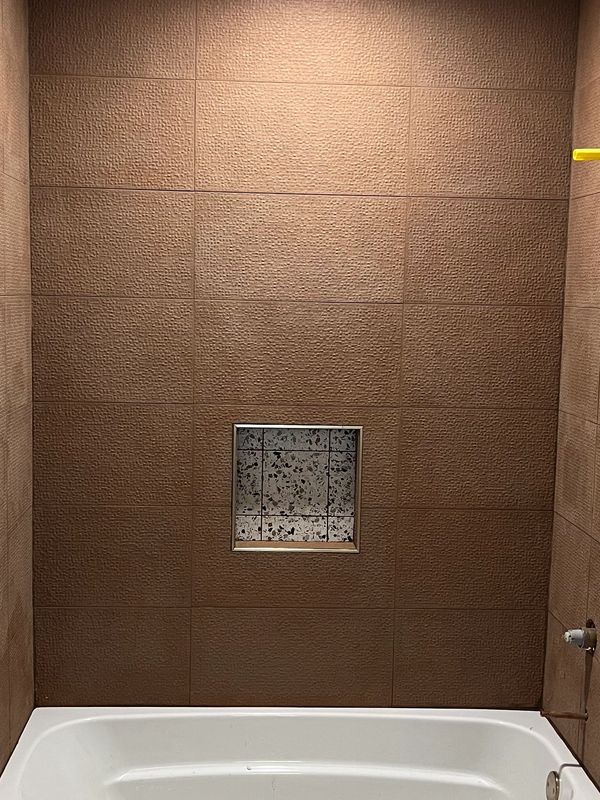 Bathtub with textured brown wall tiles and a small inset shelf.