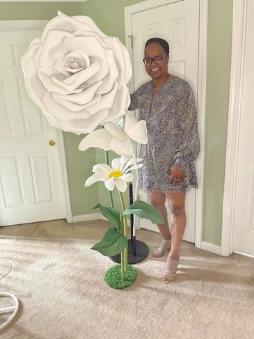 Woman posing next to an oversized white flower decoration indoors.