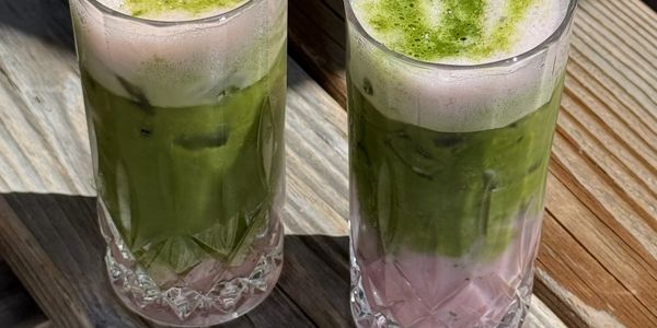 Two layered drinks with green foam and pink base on a wooden table.