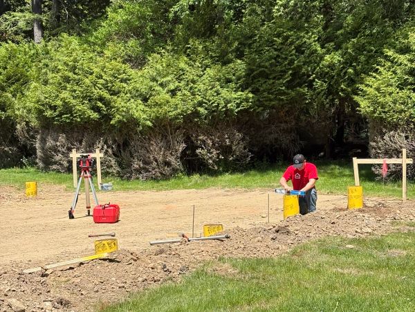 Man working on construction site with tools and greenery.