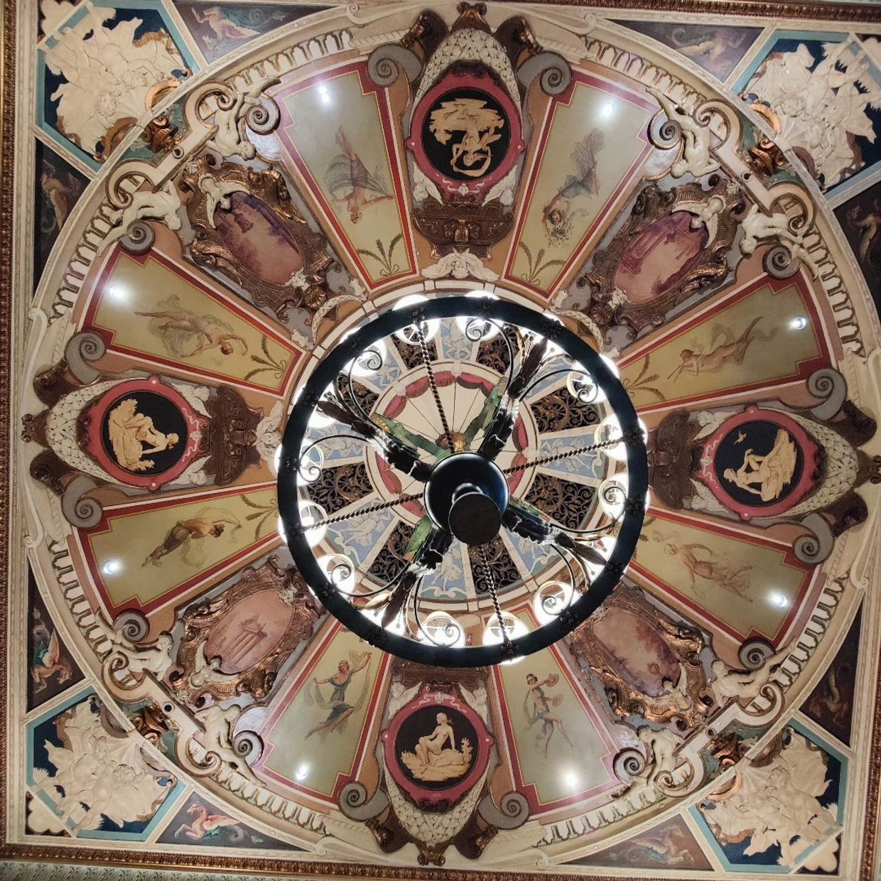 Ornate ceiling with classical paintings and a central chandelier.