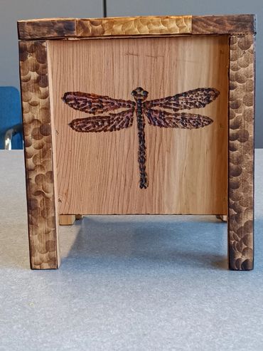 Wooden box with a dragonfly design and textured edges.