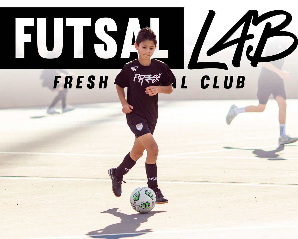 Young boy playing futsal on an outdoor court in black sportswear.