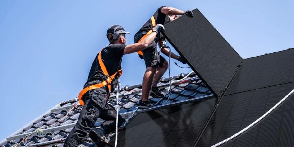 Two workers install solar panels on a rooftop under clear blue sky.