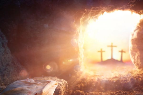 Empty tomb with a cloth and three crosses in the distance at sunrise.