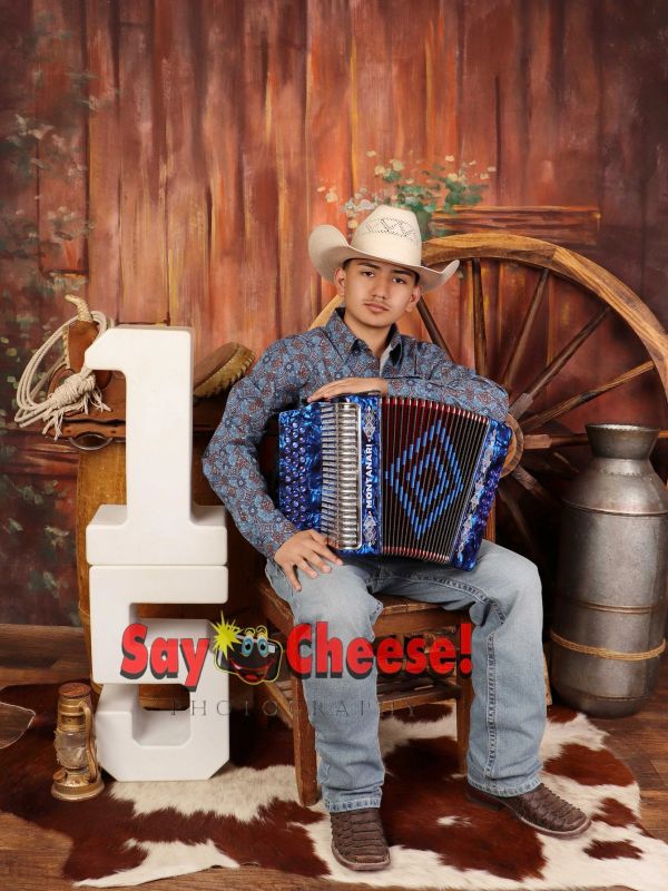 Young man in a cowboy hat playing accordion, sitting in a rustic setting with western decor.