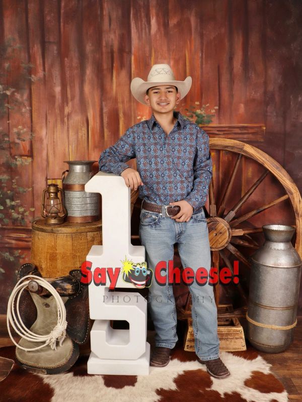 Teen boy with cowboy hat posing in rustic western-themed studio.