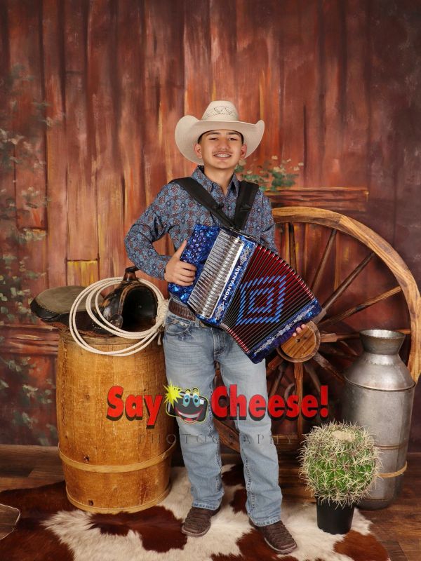 Young cowboy playing a blue accordion in a western-themed setting.