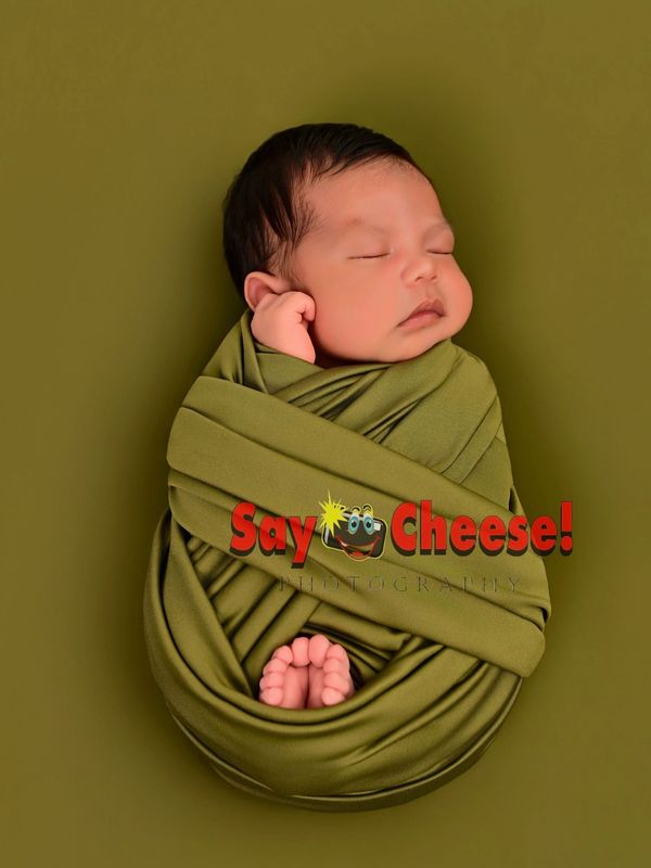 Newborn baby peacefully sleeping, wrapped in olive green fabric.