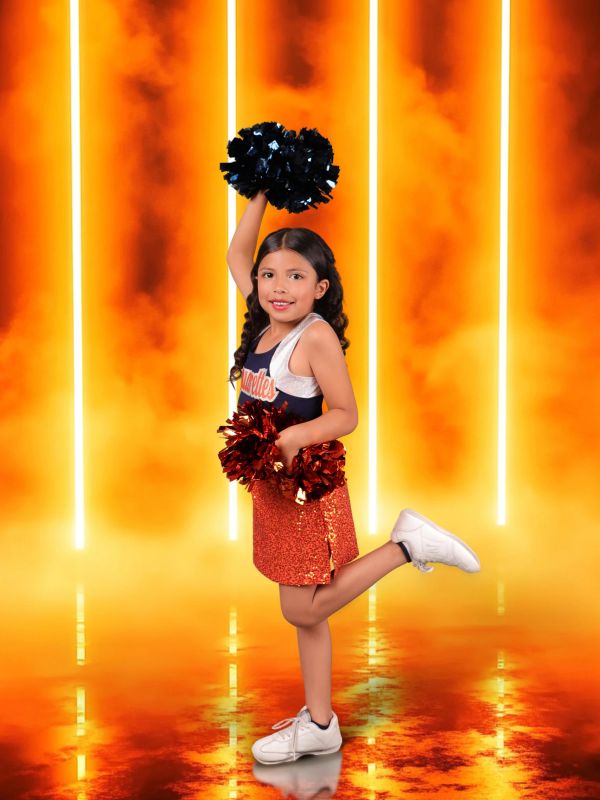 Young cheerleader posing with pom-poms against fiery background.