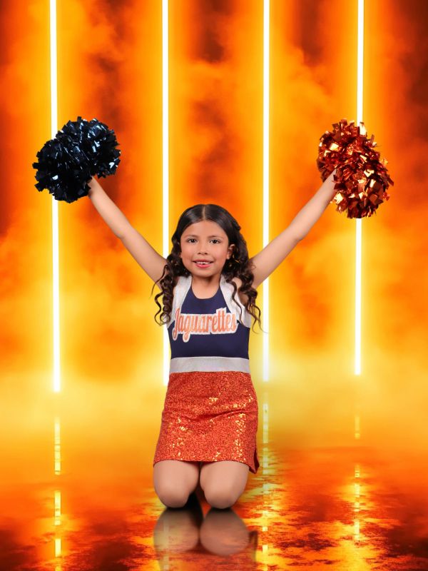 Young cheerleader kneeling with pom-poms, vibrant background.