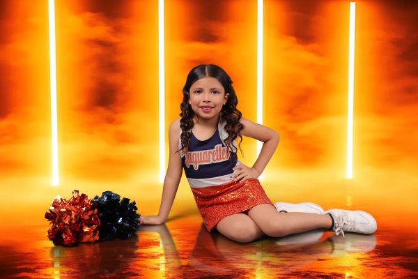 Young cheerleader posing with pom-poms in fiery background.