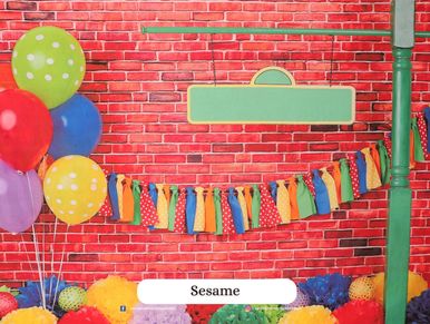 Colorful balloons and fabric garlands against a red brick wall backdrop.